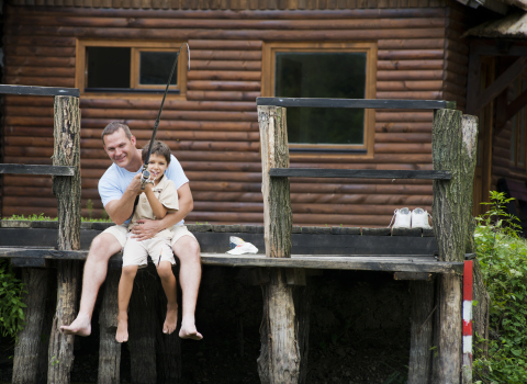father-and-son-fishing-in-front-of-their-wooden-cottage-on-water